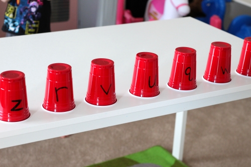 Place plastic cups with letters written on them across table in a row